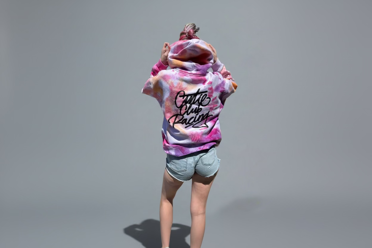 A person wearing a tie-dye hoodie with 'Cutie Club Racing' text on it, in front of a grey background.